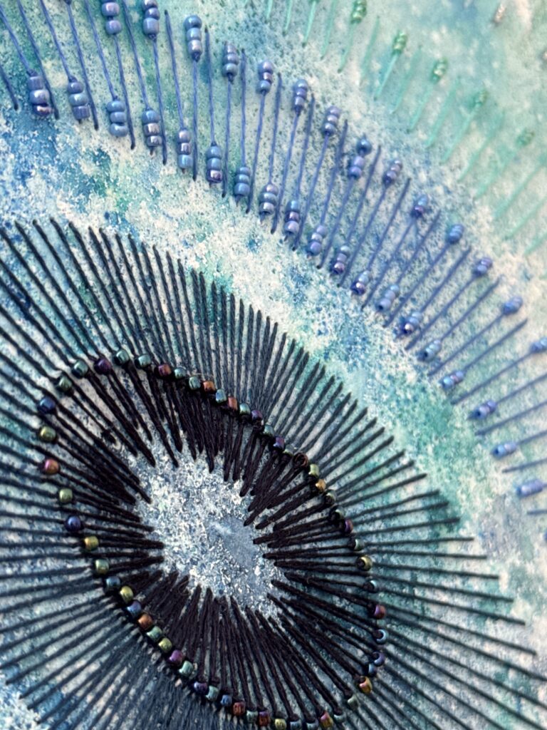 Détail d'une aquarelle brodée avec fils de coton et perles dans des tons bleus.