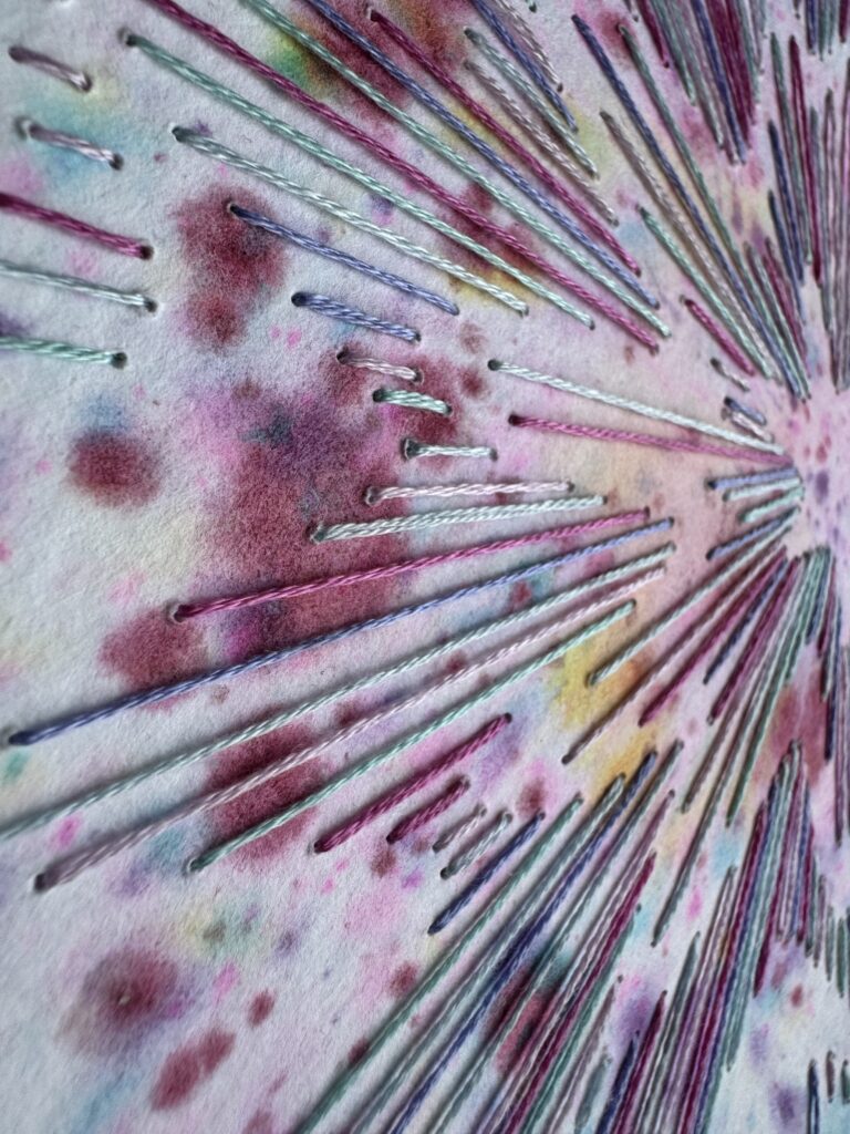 Détail d'une aquarelle brodée aux fils de coton dans des tons roses et bleus